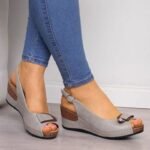 Chaussures orthopédiques talon ouvertes avec lanière portées par une femme avec un jean bleu devant un mur gris